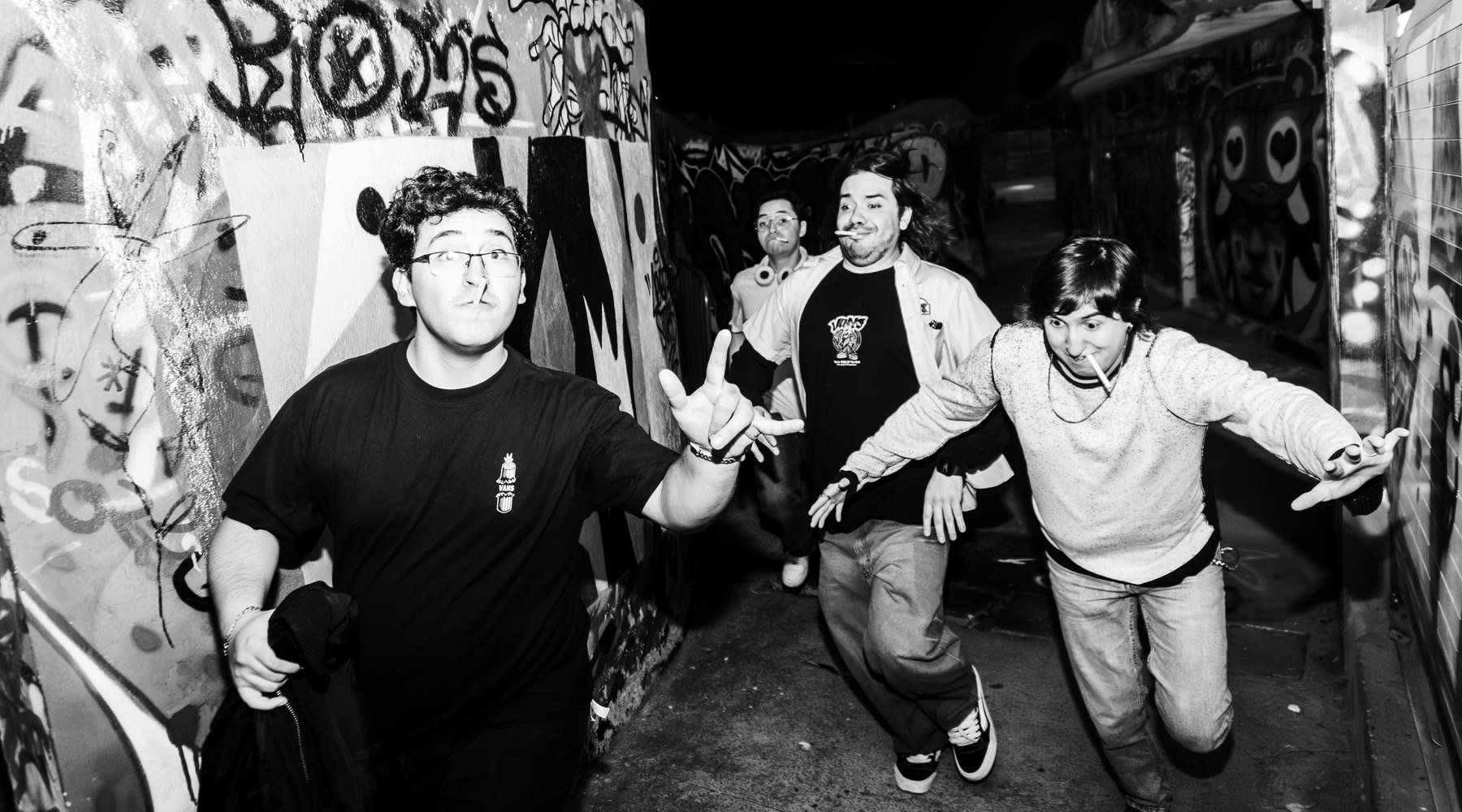 Cuatro jóvenes corriendo por un callejón con grafiti