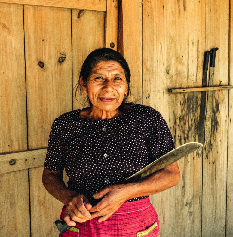 Mujer sosteniendo un machete frente a una pared de madera