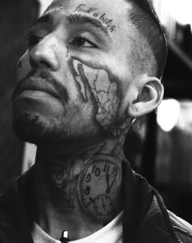 Retrato en blanco y negro de un hombre con un reloj tatuado en el cuello